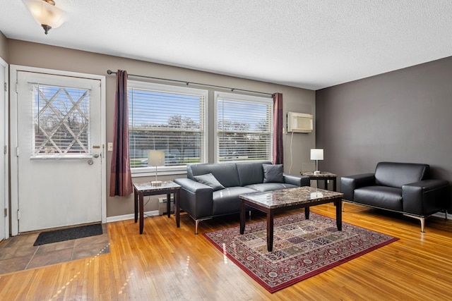 living area with light wood-style floors, a wall mounted air conditioner, a textured ceiling, and baseboards