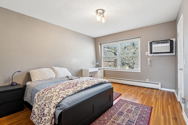 bedroom with baseboards, a baseboard heating unit, a wall unit AC, and wood finished floors