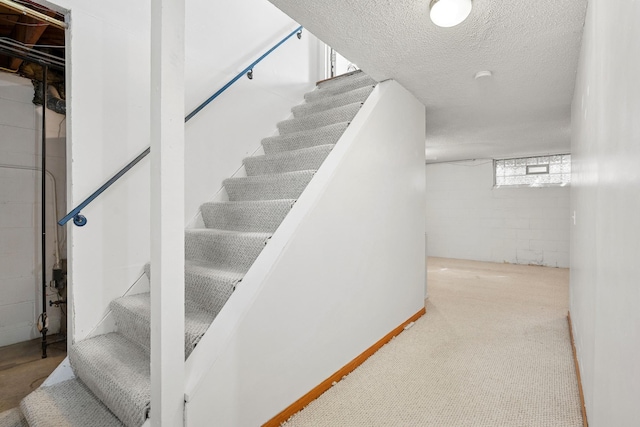 stairs with concrete block wall and a textured ceiling