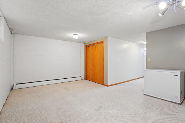 finished basement with a textured ceiling, fridge, concrete block wall, a baseboard heating unit, and light carpet
