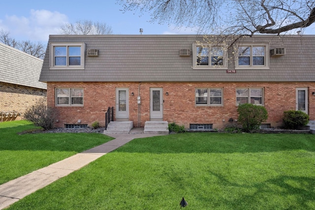 view of front facade with a front lawn, an AC wall unit, mansard roof, brick siding, and entry steps