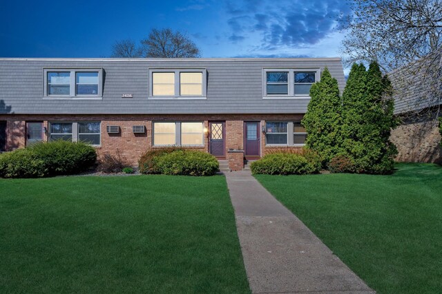 view of front of house with brick siding, mansard roof, and a front yard