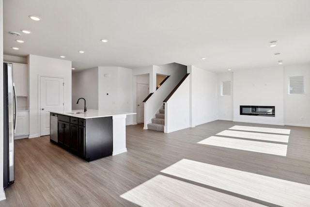 kitchen featuring a sink, stainless steel appliances, light wood-style floors, a kitchen island with sink, and light countertops
