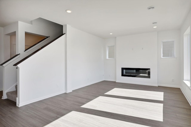 unfurnished living room featuring a glass covered fireplace, wood finished floors, stairway, recessed lighting, and baseboards