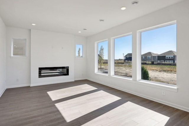 unfurnished living room featuring a glass covered fireplace, dark wood-type flooring, baseboards, and recessed lighting