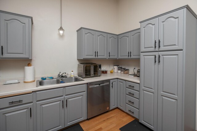 kitchen featuring gray cabinets, stainless steel dishwasher, light wood-type flooring, a sink, and light countertops