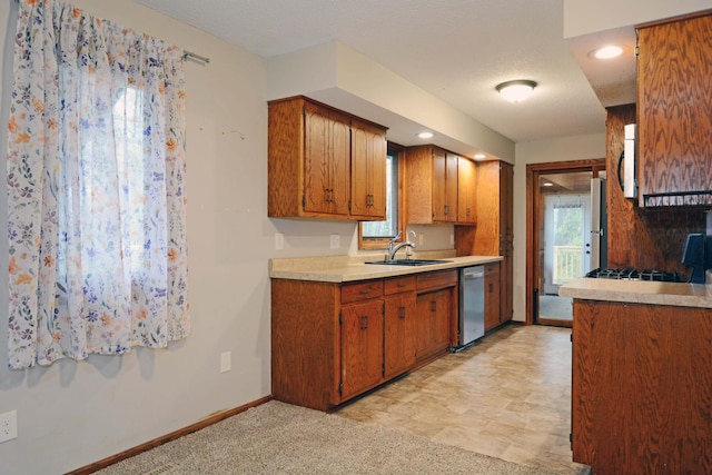 kitchen with a sink, light countertops, brown cabinetry, baseboards, and stainless steel dishwasher
