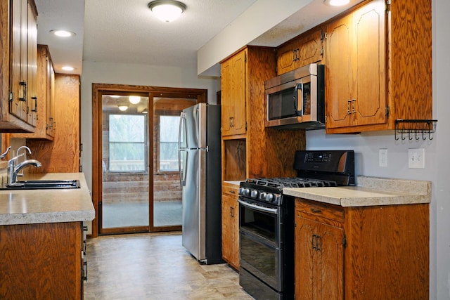 kitchen with brown cabinets, a sink, light countertops, stainless steel appliances, and recessed lighting