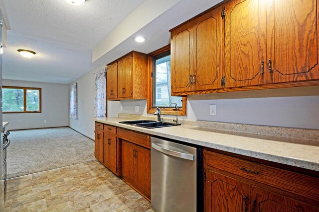 kitchen featuring brown cabinetry, light colored carpet, stainless steel dishwasher, a sink, and light countertops