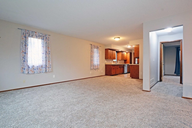 unfurnished living room featuring baseboards, light carpet, and a sink