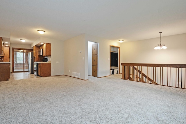 unfurnished living room with visible vents, baseboards, a notable chandelier, and light carpet