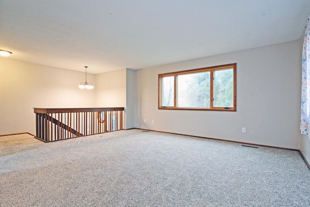 carpeted empty room with baseboards, a notable chandelier, and visible vents