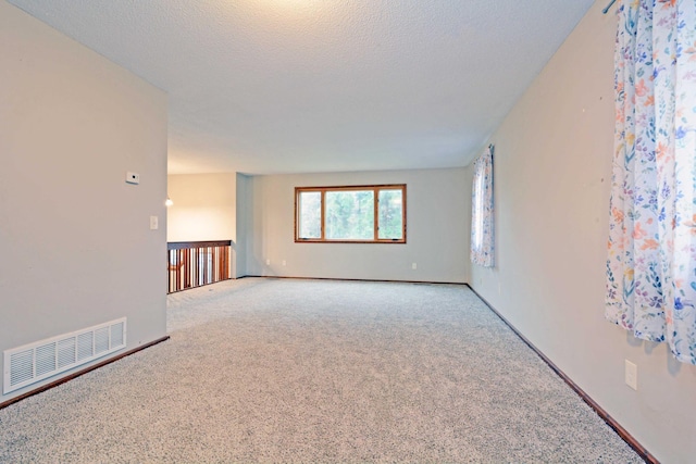 carpeted empty room with a textured ceiling, visible vents, and baseboards