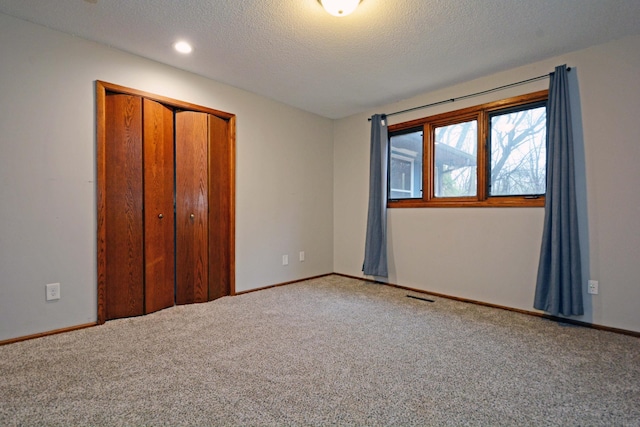 unfurnished bedroom featuring a textured ceiling, visible vents, baseboards, a closet, and carpet flooring