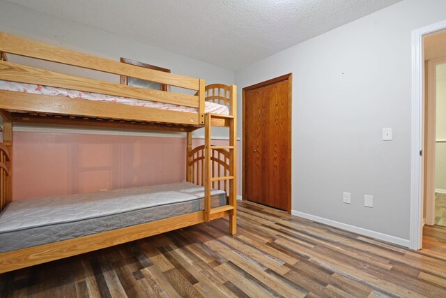 bedroom featuring baseboards, a textured ceiling, and wood finished floors