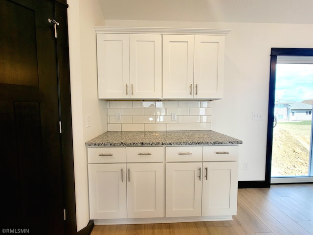 kitchen featuring decorative backsplash, baseboards, white cabinetry, light stone counters, and light wood-style flooring