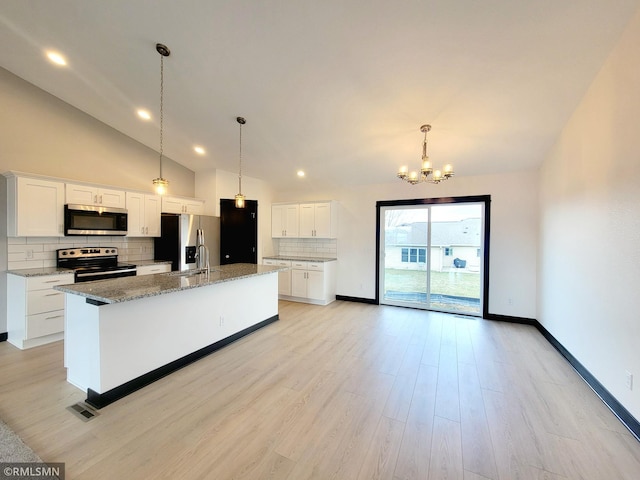 kitchen featuring light stone countertops, a kitchen island with sink, a chandelier, stainless steel appliances, and tasteful backsplash
