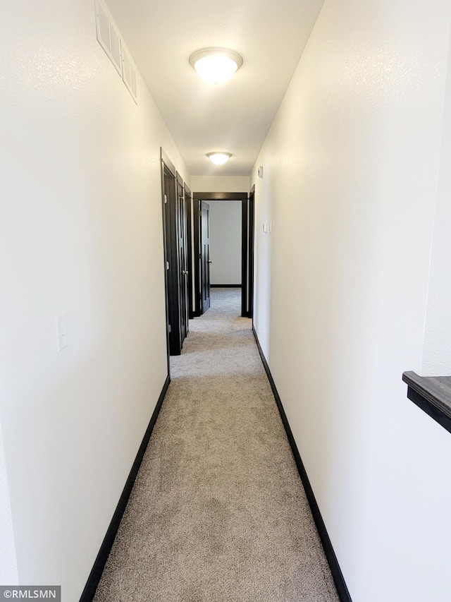 corridor featuring visible vents, baseboards, and light carpet