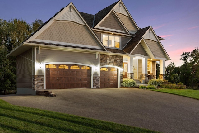 craftsman inspired home featuring a garage, driveway, stone siding, and covered porch