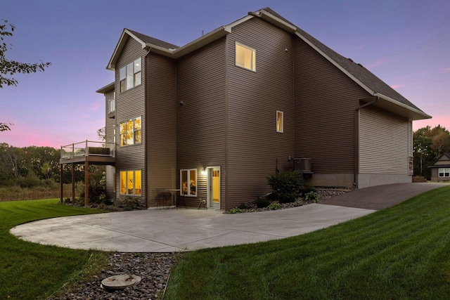 back of house at dusk with a lawn, a patio, and a wooden deck