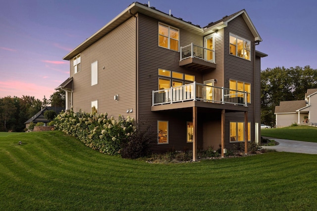 back of property at dusk featuring a lawn and a balcony