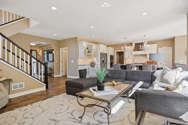 living area featuring dark wood-style flooring, a notable chandelier, arched walkways, stairs, and visible vents