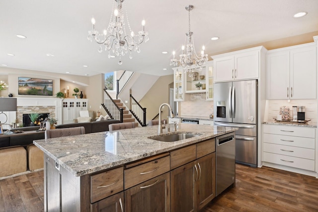 kitchen featuring dark wood-style flooring, appliances with stainless steel finishes, a sink, a notable chandelier, and an island with sink