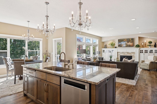 kitchen with stainless steel dishwasher, a kitchen island with sink, dark wood-type flooring, a sink, and a notable chandelier
