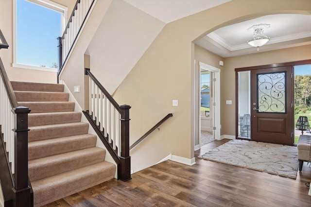 entrance foyer with crown molding, arched walkways, dark wood finished floors, and stairs
