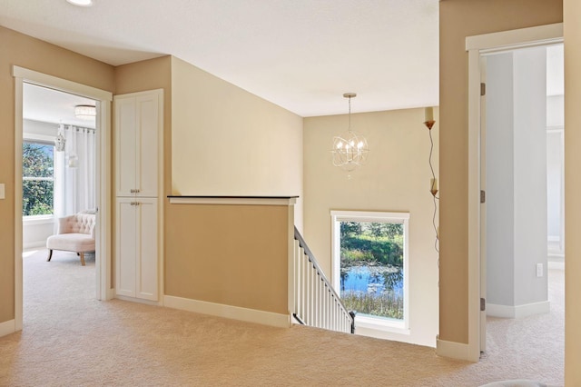 interior space featuring baseboards, carpet, a notable chandelier, and an upstairs landing