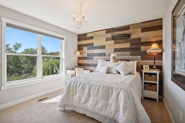 carpeted bedroom with baseboards, wood walls, an inviting chandelier, and visible vents