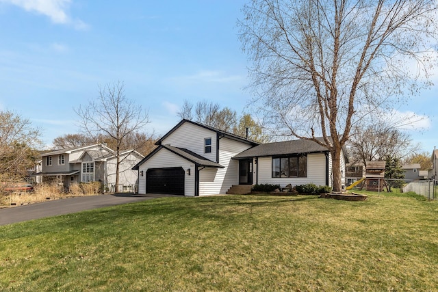 split level home with a shingled roof, aphalt driveway, fence, and a front yard