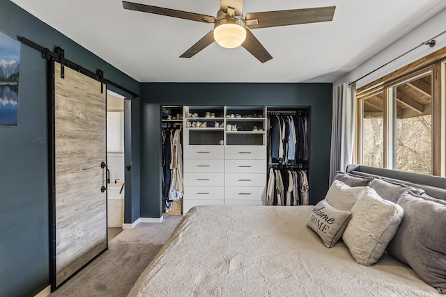 bedroom featuring a barn door, carpet floors, a ceiling fan, ensuite bathroom, and a closet