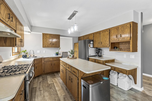 kitchen with appliances with stainless steel finishes, a sink, light countertops, brown cabinetry, and wood finished floors
