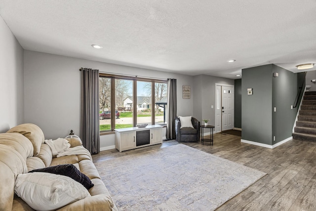 living room featuring stairway, baseboards, a textured ceiling, and wood finished floors