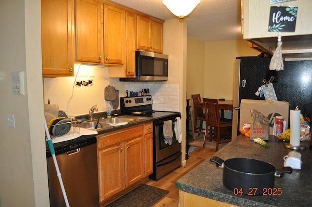 kitchen featuring appliances with stainless steel finishes, dark countertops, brown cabinets, a sink, and light wood-style floors