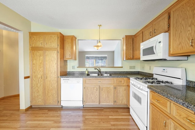 kitchen with white appliances, dark countertops, a sink, and light wood-type flooring