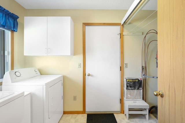 clothes washing area featuring baseboards, washing machine and dryer, and cabinet space