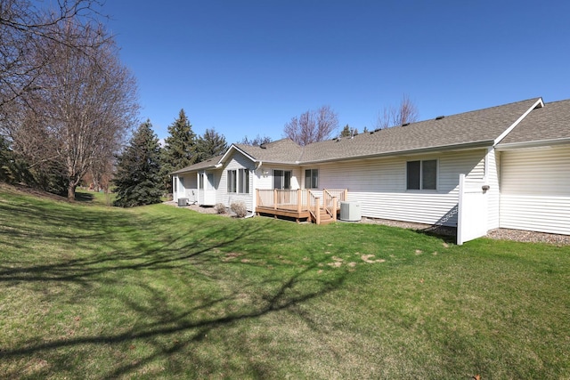 rear view of property featuring a lawn, a deck, central AC, and roof with shingles