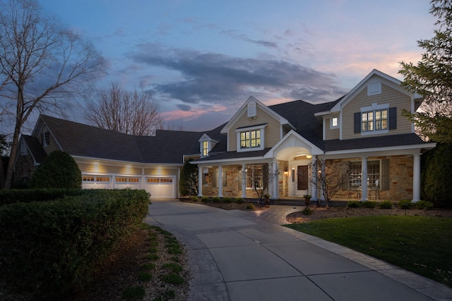 craftsman-style home with a porch, driveway, a lawn, a garage, and stone siding