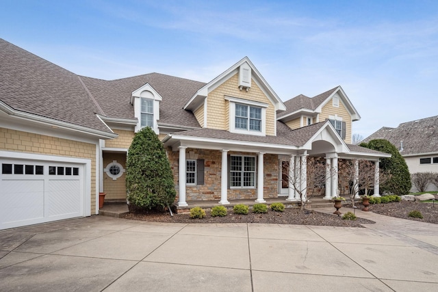 view of front of home featuring a porch, driveway, roof with shingles, a garage, and stone siding