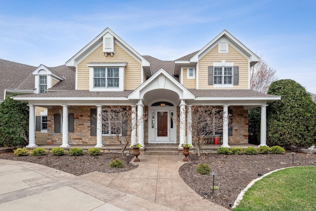 craftsman inspired home featuring a porch, a shingled roof, and stone siding