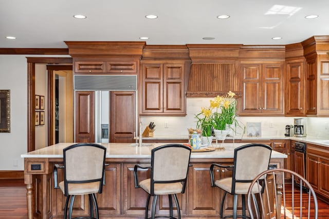 kitchen with a kitchen breakfast bar, an island with sink, recessed lighting, wood finished floors, and paneled fridge