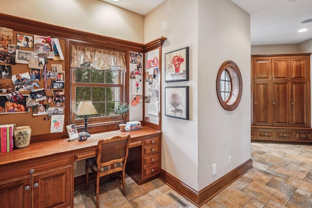 office with baseboards, stone finish flooring, built in desk, and visible vents