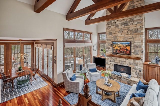living area featuring wood finished floors, beamed ceiling, a stone fireplace, baseboards, and high vaulted ceiling