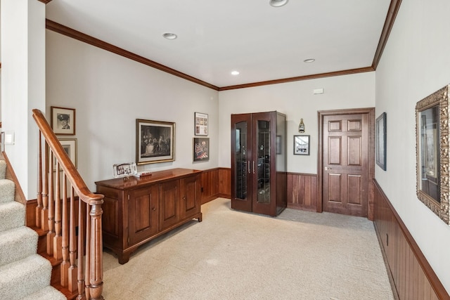 entryway featuring crown molding, light colored carpet, stairway, and a wainscoted wall