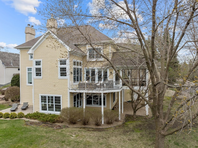 back of property featuring a shingled roof, a wooden deck, a chimney, a patio, and a yard