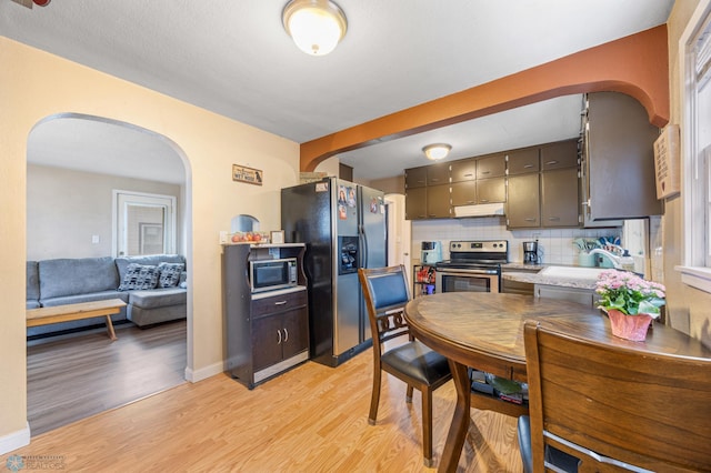 kitchen featuring light wood-type flooring, arched walkways, appliances with stainless steel finishes, and under cabinet range hood