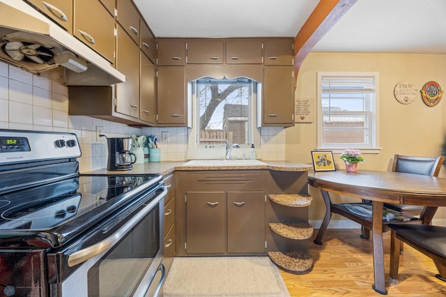 kitchen featuring light countertops, under cabinet range hood, tasteful backsplash, a sink, and stainless steel range with electric cooktop