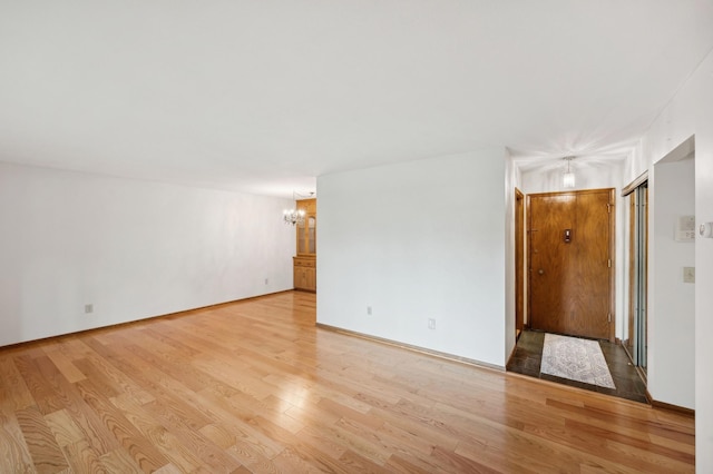 spare room featuring an inviting chandelier, baseboards, and light wood-type flooring